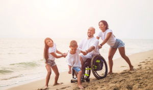 Father in a wheelchair with family on the beach